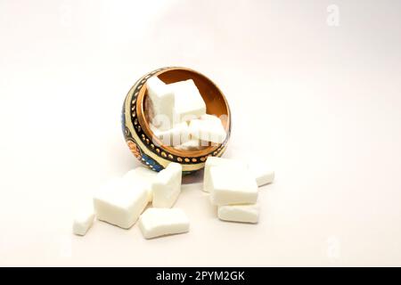 Eine Nahaufnahme von weißen Zuckerwürfeln in einer kunstvoll verzierten Schüssel auf weißem Hintergrund Stockfoto
