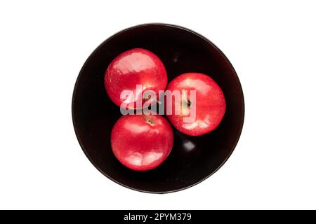 Drei rote Äpfel in einer schwarzen Keramikplatte auf weißem Hintergrund, Draufsicht. Stockfoto