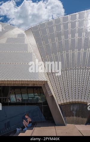 Eine junge Frau, die im Schatten des Opernhauses sitzt, um ihr Smartphone zu benutzen, Sydney, New South Wales, Australien Stockfoto
