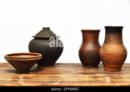 Töpfe, Schüsseln und Krüge aus altem Steingut auf einem Holztisch auf weißem Hintergrund. Set aus Tonkanne, Schüssel und Töpfen Stockfoto