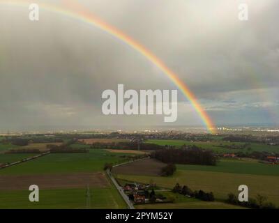 Dieses Bild zeigt einen atemberaubenden Blick auf einen Regenbogen, der sich über eine malerische Ackerlandschaft erhebt Stockfoto