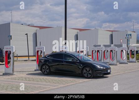 Mondovi, Italien - 18. April 2023: Statische Aufnahme eines soliden schwarzen Tesla Model 3 Dual Motor, der an einem sonnigen Frühlingstag am Mondovi Supercharger aufgeladen wird. S Stockfoto