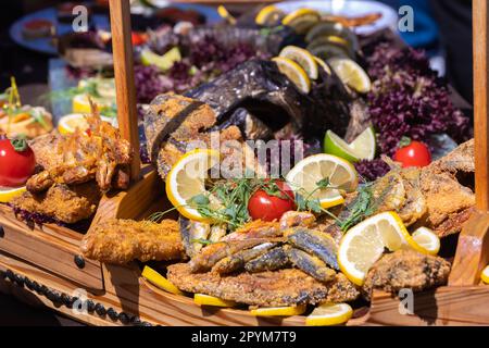 Nahaufnahme eines gebratenen Sklaven mit Zitronenscheiben, Tomaten auf dem Tisch an einem sonnigen Tag. Fischfestival, Street Food. Stockfoto