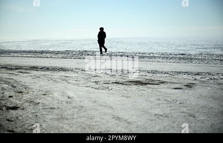 Tuktoyaktuk, Kanada. 27. April 2023. Ein Mann geht am Rand des Polarmeers in Tuktoyaktuk, Arktis entlang. Kredit: Britta Pedersen/dpa/Alamy Live News Stockfoto