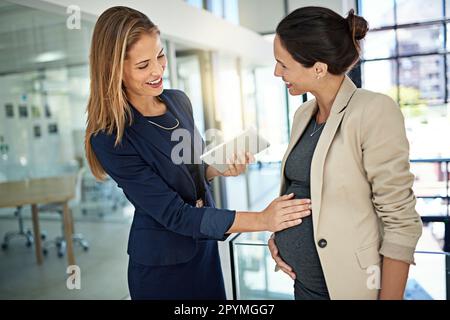 Ihr Urlaub muss jeden Tag beginnen. Eine Frau, die mit einem Kollegen über ihre Schwangerschaft spricht, während sie in einem modernen Büro steht. Stockfoto