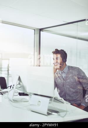 Sich um die Kunden zu kümmern. Aufnahme eines attraktiven jungen Geschäftsmanns mit Headset, während er an seinem Schreibtisch sitzt. Stockfoto