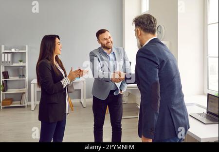 Zwei lächelnde männliche Geschäftspartner, die sich im Amt die Hand schütteln Stockfoto
