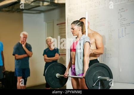 Trainiere wie eine Bestie, sehe wie eine Schönheit aus. Eine Frau, die Gewichte hebt, während eine Gruppe im Hintergrund zusieht. Stockfoto