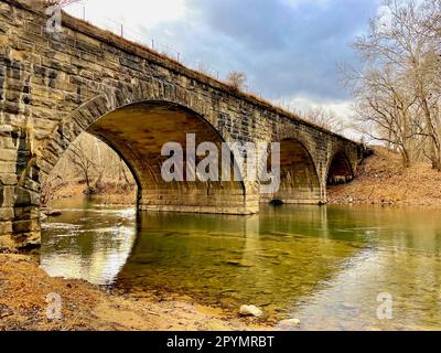 Der Cacapon River fließt unter einer historischen Steinbrücke, die von Güterzügen und Amtrak-Zügen in der Nähe des Potomac River genutzt wird. Stockfoto