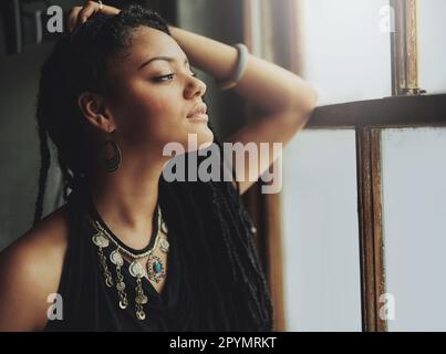 Die Aussicht genießen. Eine attraktive junge Frau, die am Fenster steht. Stockfoto