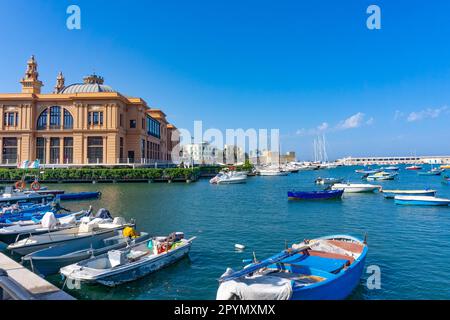 Breite Landschaft des Margherita-Theaters mit Fischerbooten im alten Hafen von Bari, Apulien, Italien. Eine farbenfrohe Landschaft mit blauem, klarem Wasser. Stockfoto