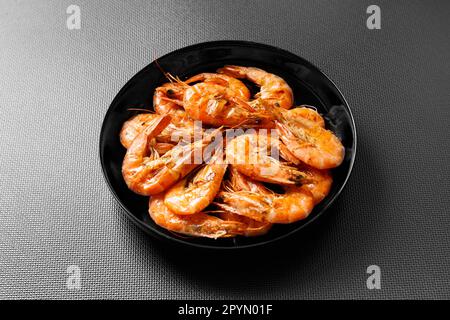Gebratene Garnelen auf einem schwarzen Teller auf einem dunklen Keramiktisch. Garnelengrill auf dunklem Hintergrund. Stockfoto