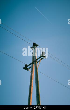 Eine vertikale Aufnahme eines hölzernen Telefonmastes mit niedrigem Winkel steht vor einem klaren blauen Himmel Stockfoto