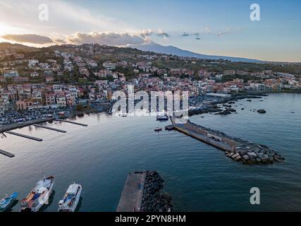 Atemberaubende Drohnenaufnahme von Acitrezza mit malerischem Hafen, Pier und majestätischem Ätna im Hintergrund. Stockfoto