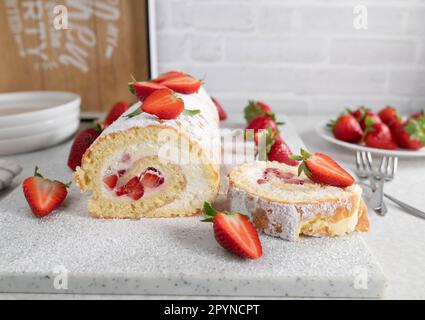 Schweizer Rolle mit Schlagsahne und Erdbeerfüllung auf hellem Küchenhintergrund Stockfoto