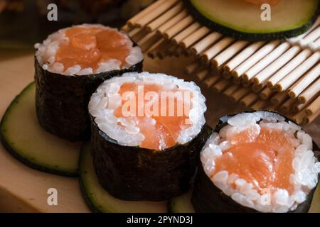 Nahaufnahme köstlicher Lachs-Sushi-Brötchen auf Avocado-Scheiben, umgeben von zusätzlicher Avocado und künstlerischer Bambus-Präsentation. Stockfoto