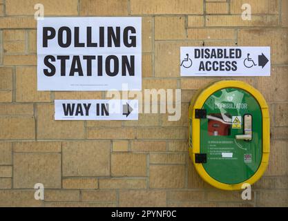 Eine Mauer mit einer Vielzahl von Hinweisschildern, darunter ein markantes Schild mit der Aufschrift „Polling Station“, weist die Leute darauf hin, wo sie bei einer Wahl wählen können. Darunter Stockfoto