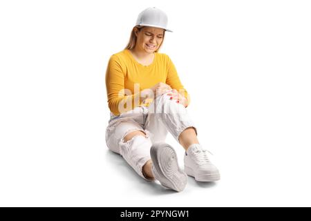 Junge Frau, die auf dem Boden sitzt und ihr schmerzhaftes Knie isoliert auf weißem Hintergrund hält Stockfoto