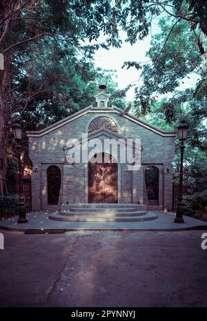 NakhonSawan, Thailand - 23. April 2023 - Antike eiserne Bogentür an einer Ziegelsteinwand in einem historischen Backsteingebäude, umgeben von Straßenlaternen Stockfoto