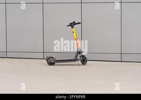 Ein gelb-schwarzer Elektroroller steht neben einer grauen Wand Stockfoto