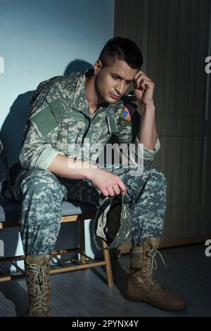 Frustrierter amerikanischer Militärveteran in Uniform, der nachts zu Hause im Flur sitzt, Börsenbild Stockfoto