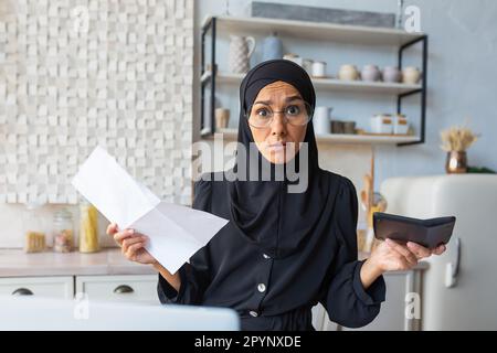 Junge besorgte muslimische Frau in Hidschab mit Dokumenten und Taschenrechner. Finanzielle Probleme mit Konten, Krediten, Familienbudget. Er sieht leider auf die Ca Stockfoto