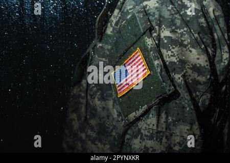 Freigestellte Ansicht eines amerikanischen Soldaten in Militäruniform mit Flagge hinter einem regnerischen Fenster, Stockbild Stockfoto