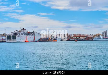 Die Fähre fährt in den Hafen von Cadiz mit einem festsitzendem Schiff und Gebäuden der Altstadt im Hintergrund, Cadiz, Spanien Stockfoto