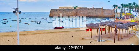 Panorama des Sandstrands La Caleta mit kleinen Fischerbooten am Ufer der Bucht von Cadiz und der Burg Santa Catalina im Hintergrund, Spanien Stockfoto