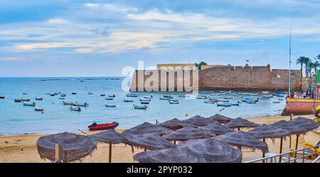 Panorama der Bucht von Cadiz mit Strohschirmen am Strand von La Caleta und Steinbastionen der Burg Santa Catalina im Hintergrund, Cadiz, Spanien Stockfoto