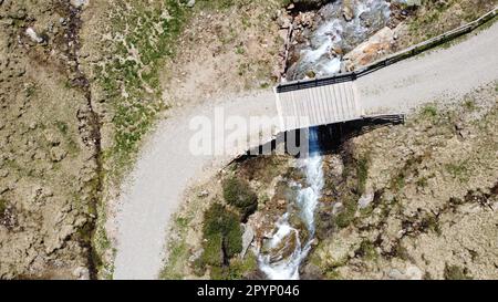 Kleine Hölzerne Brücke über einen Bergbach, über eine schmale Bergstraße zu den nahegelegenen Almen führt Stockfoto