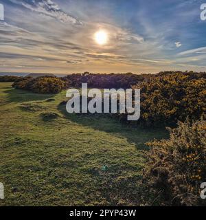 Auf diesem atemberaubenden Foto geht die Sonne hinter dem berühmten Worm's Head unter und strahlt ein goldenes Licht über die ruhige walisische Küste. Der Himmel darüber ist ein Stockfoto