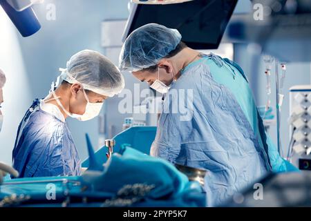 Das Team von Chirurgen im Operationssaal hat sich über den Patienten gebeugt, komplexe chirurgische Operationen, High-Tech-Medizin, lebensrettend. Stockfoto