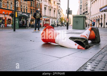 Ein orange-weiß gestreifter Verkehrskegel, der auf dem Bürgersteig in einer urbanen Umgebung ruht Stockfoto