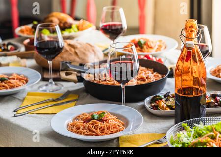 Tischdecken eines Restaurants mit selektivem Fokus auf einem Teller Spaghetti mit Tomatensauce. Flasche und Gläser Rotwein im und Bio-Lebensmittel Stockfoto