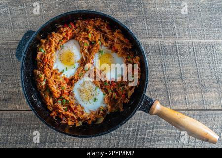 Kohl mit Gemüse und Spiegeleiern in einer Pfanne auf Holzhintergrund, Nahaufnahme, Draufsicht. Lebensmittelhintergrund. Gesundes Essen Stockfoto