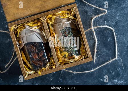 Glasbecher mit Blumentee und Glasbecher mit Kiefernkonfitüre in einer hölzernen Geschenkbox auf einem Tisch, Nahaufnahme. Schönes Geschenk für Familie und Freunde Stockfoto