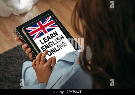 Online-Lernkonzept. Eine Frau hält ein Tablet in der Hand auf dem Bildschirm, auf dem es geschrieben ist – Learn English Online Stockfoto