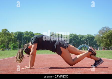 Junge argentinische latina, dehnt ihre Körpermuskulatur und wärmt sich auf, bevor sie mit dem Training auf der Laufbahn, dem Sportkonzept, dem Kopierbereich beginnt. Stockfoto