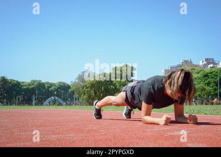 Junge latina in schwarzer Sportbekleidung, trainiert mit Brettermuskeln auf der Laufbahn, Sportkonzept, Kopierraum. Stockfoto