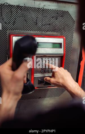 Person, die eine Telefonnummer an einem öffentlichen Telefon in einer Münztelefonkabine wählt. Telekommunikationstechnologie der alten Schule. Stockfoto