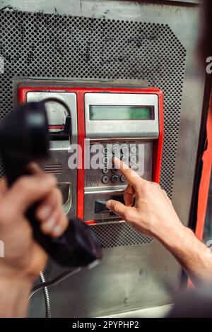 Person, die eine Telefonnummer an einem öffentlichen Telefon in einer Münztelefonkabine wählt. Telekommunikationstechnologie der alten Schule. Stockfoto