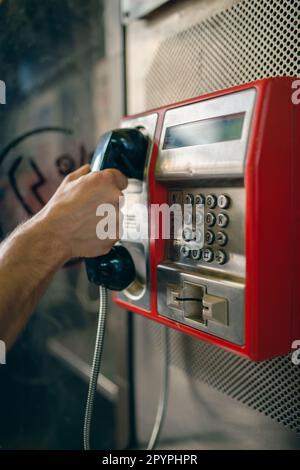 Person, die eine Telefonnummer an einem öffentlichen Telefon in einer Münztelefonkabine wählt. Telekommunikationstechnologie der alten Schule. Stockfoto