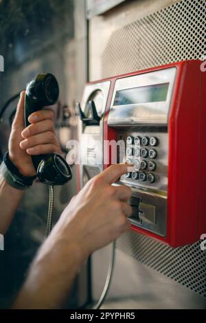 Person, die eine Telefonnummer an einem öffentlichen Telefon in einer Münztelefonkabine wählt. Telekommunikationstechnologie der alten Schule. Stockfoto