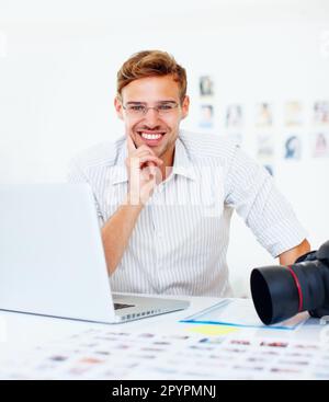 Lächelnder Fotograf. Porträt eines jungen Fotografen, der ein Notebook benutzt und Ihnen ein attraktives Lächeln gibt. Stockfoto