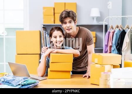 Ein junges asiatisches Paar, das in einem Hausbüro arbeitet, sieht aus wie ein Startup-Unternehmen, das glücklich und positiv lächelt. Stockfoto