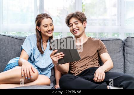 Glückliches Paar, das ein Tablet benutzt, auf den Tablet-Bildschirm eines digitalen Computers schaut und sich auf dem bequemen Sofa entspannt. Liebes Paar, das online einkauft Stockfoto