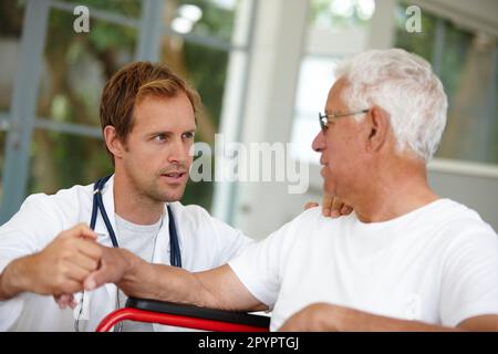 Er sorgt sich wirklich um seine Patienten. Ein gutaussehender Arzt, der mit seinem älteren Patienten im Rollstuhl spricht. Stockfoto