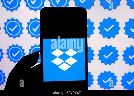 In dieser Fotoabbildung wird auf einem Smartphone ein Dropbox-Logo mit dem blauen Häkchen-Logo im Hintergrund angezeigt. Stockfoto