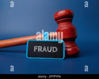 Hammer und Holzbrett mit dem Wort BETRUG auf blauem Hintergrund. Stockfoto